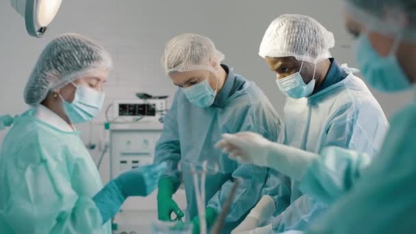 オペレーティングルームで医療機器を使用した明るいランプの下で心臓移植手術を実施する制服の専門外科医と看護師のグループ — ストック動画