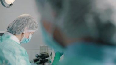 Bir grup melez profesyonel cerrah ve üniformalı hemşireler ameliyathanede tıbbi gereçler kullanarak parlak lambalar altında kalp nakli ameliyatı yapıyorlar.