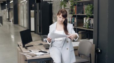 Fayans galerisinde masasının yanında tasarım projesi olan mavi takım elbiseli kadın tasarımcı.