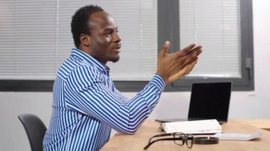 Konsantre olmuş Afrikalı yönetici modern ofiste oturup konuşuyor. Çalışanlar iş meselelerini düşünür, arama çözümü bulur, internette finans araştırması yapar, yaratıcı telgraflar yazar.