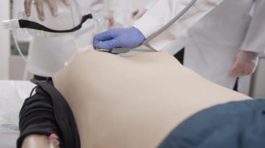 İlk yardım eğitimi. Bebeğin yüzünde oksijen maskesi var. Bir doktor hastanın akciğerlerini dinler.