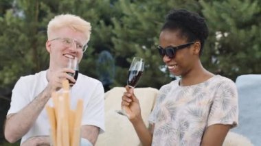 İki arkadaş, biri sarı saçlı, gözlüklü, diğeri siyah saçlı, güneş gözlüklü, yaz pikniğinin tadını çıkarıyorlar.