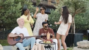 Arkadaşlar güneşli bir öğleden sonra doğanın tadını çıkarıyor, dans ediyor ve gitar çalıyorlar.