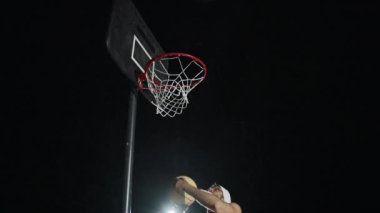 Adam açık hava sahasındaki parlak ışıkların altında gece yarısı basketbol maçından zevk alıyor.