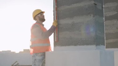 İnşaat işçisi, gün batımında yüksek bir inşaat sahasında duvar hizalaması için bir seviye aracı kullanıyor