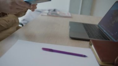 Verimli bir öğleden sonra seansında, not alırken ve dizüstü bilgisayar kullanırken masasında çalışan bir kadın.