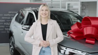 Kadın, galeride yaylı bir arabanın yanında durmuş test sürüşlerini ve alışverişlerini destekliyor.