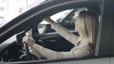 Kadın bir araba galerisinde yavaş çekimde test sürüşü yapmaktan zevk alıyor.