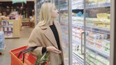 Kız süpermarkette alışveriş yaparken telefonundaki eşyaları yavaş çekimde kontrol ediyor.