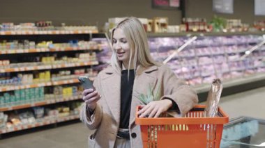 Yavaş çekimde çeşitli market ve ürünlerle dolu bir markette akıllı telefon kullanan bir kız.
