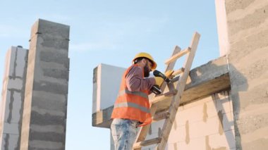 Bir inşaat sahasında matkapla çalışan koruyucu yelekli bir adamın yavaş çekimi.