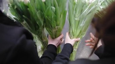 Renkli bir çiçek pazarında taze lale buketleri tutan ellerin yavaş çekimde yakalanması.