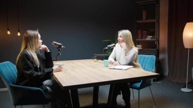 Podcast stüdyosunda gitar ve modern dekorun yer aldığı iki kadın arasındaki iş görüşmesi.