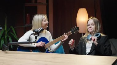 Podcast stüdyosunda iki kadın arasında gitar ve mikrofonla sohbet.