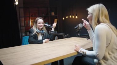 Podcast stüdyosunda mikrofon ve gitarlarla iki kadın arasında tartışma.