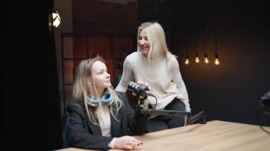 Podcast stüdyosunda iki kadın arasında mikrofon ve gitar eşliğinde sohbet.