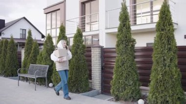 Teslimatçı kadın, banliyö mahallesinde elinde paketle eve geliyor.
