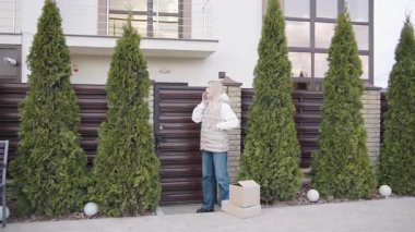 Teslimatçı kadın elinde bir paket tutarken evin dışında konuşuyor.