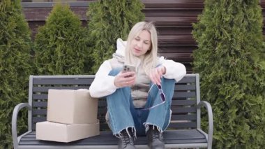 Kadın evinin önünde oturmuş paketleri beklerken teslimat durumunu kontrol ediyor.