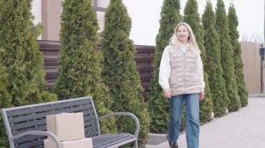 Teslimatçı kadın yeşilliklerle çevrili bir yerleşim bölgesinde kutu taşırken eve yaklaşıyor.