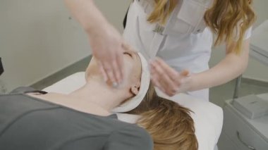 Ağır çekimde kalıcı güzellik etkisi için kozmetoloji tedavisi gören bir kadın yüz maskesi uygulaması alıyor.