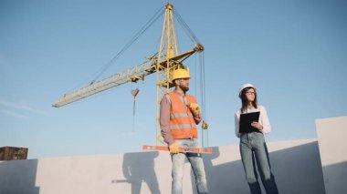 İnşaat ekibi, arka planda vinç olan bir inşaat alanında proje ilerlemesini tartışıyor