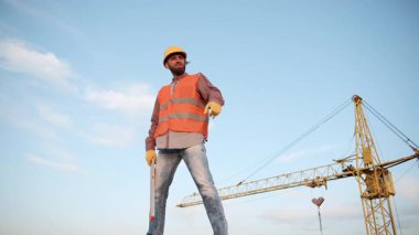 İnşaat işçisi, gündüz saatlerinde vinci arka planda güvenli bir şekilde duruyor.