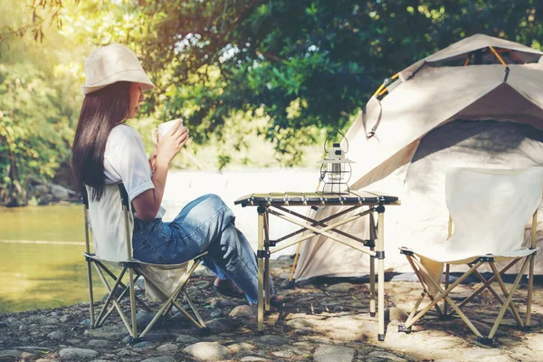 Camping outdoor. Asian women camping leisure and destination travel near waterfall. People hand holding cup and drinking coffee on the tents in morning. Tourism relax and chill in summer holiday