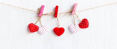 Valentines Day. Sewed pillow hearts row border on red and white clothespins at rustic white wood planks. Happy lovers day card mockup, copy space for banner. Valentine Concept 