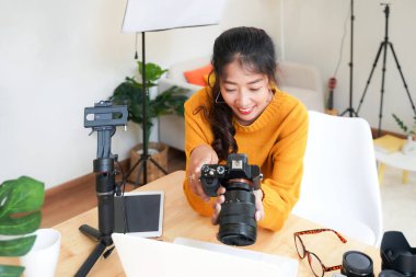 Yaşam tarzı Asya 'lı genç kadın fotoğrafçı ve merkez ofiste elinde bir DSR kamera tutan serbest çalışan. Stüdyoda yeni bir projede gülümseyen kadın fotoğrafçı