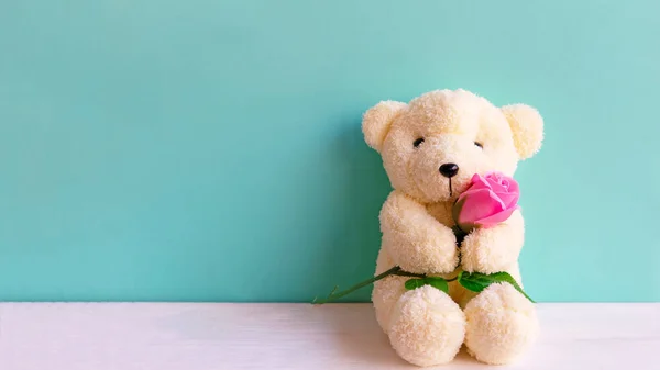 Cute teddy bear holding pink rose in its arms on wooden green background, copy space. Valentine Concept