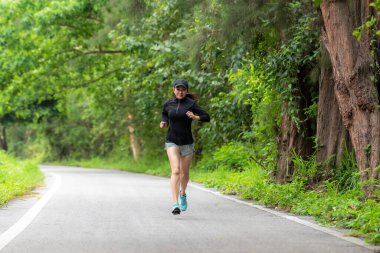 Sağlıklı bir kadın dışarıda koşuyor ve antrenman yapıyor. Asyalı koşucular spor salonu, spor salonu, doğa parkı geçmişi. Sağlık ve Yaşam Tarzı Konsepti