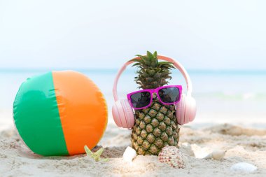 Partide yaz mevsimi. Güneş gözlüklü hippi Pineapple Fashion ve kumsalda güzel mavi gökyüzü arka planında top plajlı müzik dinlemek. Tropikal stil için yaratıcı sanat meyvesi