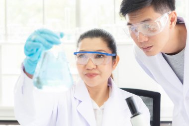 Asyalı kadın ve erkek bilim adamları çalışma verilerini analiz ediyor ve atölye için mikroskop başarısını değerlendiriyor. Sağlık araştırmacıları yaşam bilimi laboratuvarında damlatan kimyasallarla ilgili bir araştırma yapıyor.