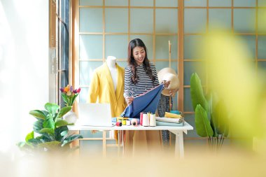 Asian young women fashion designer  working on her designer in the showroom,  Lifestyle Stylish tailor clothing design and cutting cloths in studio.  Business small Concept