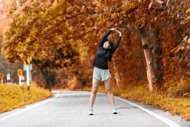 Sağlıklı bir kadın serinledikten sonra rahatlar ve dışarıdaki yola bakar. Asyalı koşucu kadın spordan sonra spor yapıyor ve sonbaharda parkta koşu yapıyor. Sağlıklı ve Yaşam Tarzı Konsepti