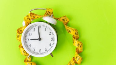 Sağlıklı aralıklarla oruç tutmak için diyet ve kilo kaybı. Ölçümlü musluğu olan çalar saat. Diyet ve Sağlıklı Konsept, yeşil renk arkaplanı, metin için kopyalama alanı