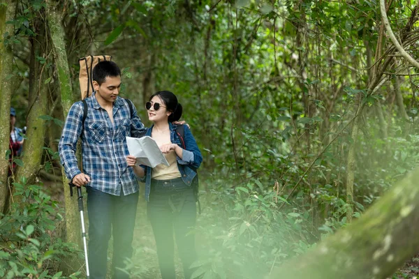Asian couple traveler with backpack adventure holding map to find directions and walking relax in the jungle forest outdoor for destination leisure explore education nature on vacation. Travel and Lifestyle Concept