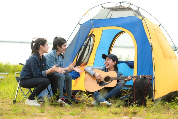Camping outdoor. Group  friends camping leisure and destination travel. Family sitting around camp fire and playing guitar and roasted sausages, tourism relax and travel near river in holiday.
