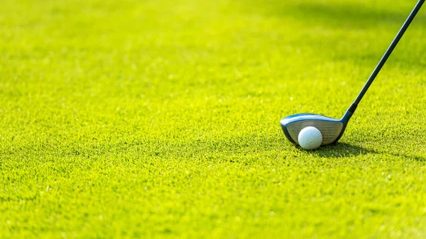 Close up Golf club hitting golf ball along with tee on green tee. Lifestyle and Healthy Concept. Copy space for banner