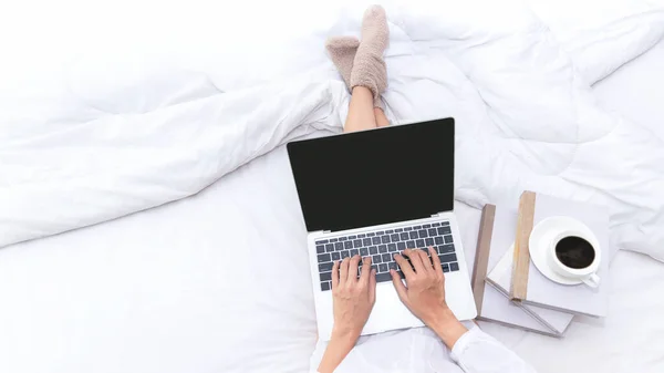 Businesswomen working on laptop and drinking coffee in morning relax mood in winter season. Close up legs women on white bed in the bedroom. Lifestyle Concept, copy space for banner