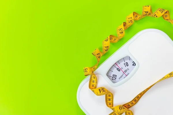Weight loss control planning.  White scale and measuring tape for body dieting healthy life.  Green background. Top view copy space for banner