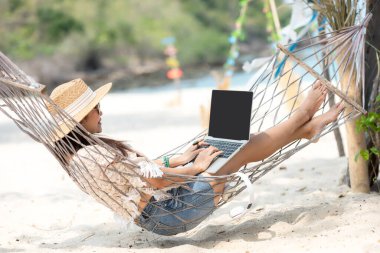 Hayat tarzı serbest çalışan bir kadın dizüstü bilgisayar kullanıyor ve sahilde rahatlıyor. Asyalıların başarısı ve birlikte iş meşgaleniz ve tatilde internette konferansınız.