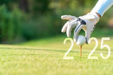 Kapalı el golfçüsü kadın yeni sağlıklı bir yaşam için yeşil golfe Mutlu Yeni Yıl 2025 için golf topu koyuyor. kopyalama alanı. Sağlıklı ve Tatil Konsepti