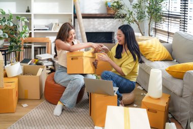 Genç kadınlar ve arkadaşları yeni evlerinde mutlu ve birlikte kutuları paketlerken eve taşınmaya yardım ediyorlar. Asyalı kadınlar aileleriyle yaşamak için gayrimenkul yatırımı yapıyorlar