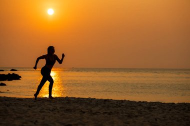 Siluet atletik kadın egzersiz yapıyor ve kumsalda özgürce koşuyor. İnsanlar gün batımında koşup antrenman yapıyor. Yaşam Tarzı ve Sağlıklı Kavram. 