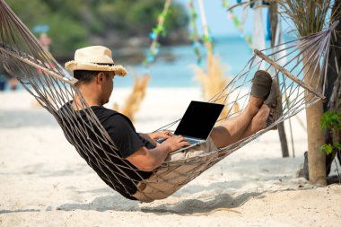 Hayat tarzı serbest çalışan bir adam, dizüstü bilgisayar kullandıktan sonra plajda rahatlayıp hamakta uyur. Asyalıların başarısı ve birlikte iş meşgaleniz ve tatilde internette konferansınız.