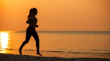 Siluet atletik kadın egzersiz yapıyor ve kumsalda özgürce koşuyor. İnsanlar gün batımında koşup antrenman yapıyor. Yaşam Tarzı ve Sağlıklı Kavram.