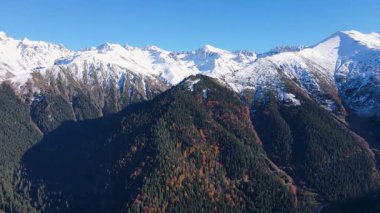 Karla kaplı dağların, ormanların ve sonbahar renklerinin görüntüleri.