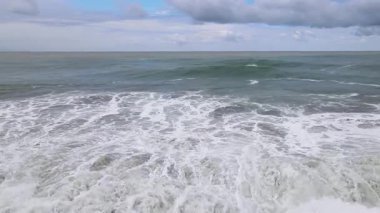 Parlak beyaz dalgaların ve bulutlu gökyüzünün görüntüsü.